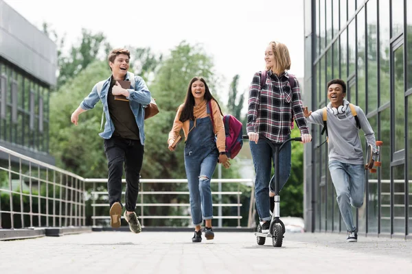 Adolescentes felices y positivos sonriendo, corriendo y montando scooter - foto de stock