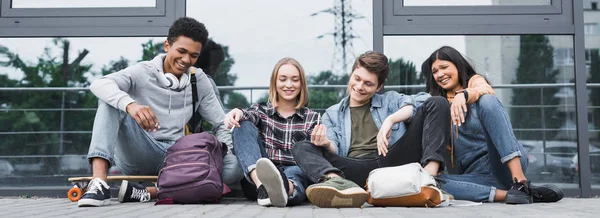 Panoramic shot of happy friends smiling, sitting and smoking — Stock Photo