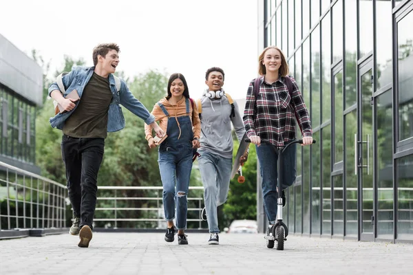 Fröhliche und verspielte Teenager, die lächeln, laufen und Roller fahren — Stockfoto