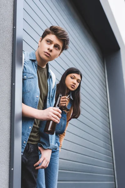 Boy and brunette teenager looking away, smoking cigarette and drinking beer — Stock Photo