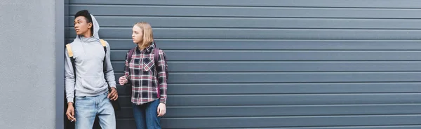 Panoramic shot of african american boy and blonde teenager looking away, smoking cigarettes and holding beer — Stock Photo