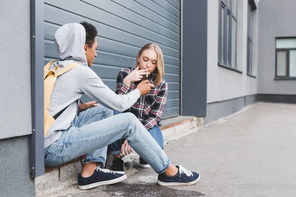 African american boy lighting cigarette of blonde and pretty teen — Stock Photo