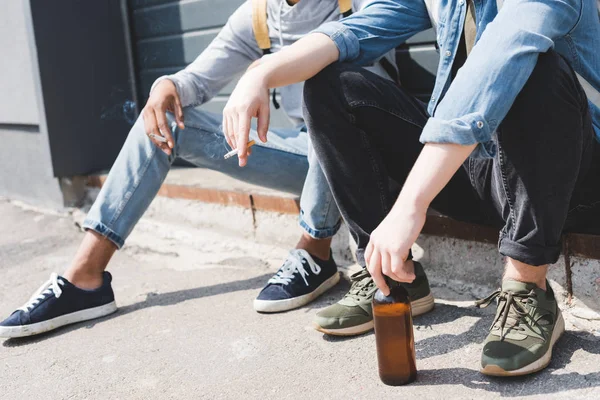 Vista cortada de meninos sentados, segurando cerveja e fumando cigarros — Fotografia de Stock