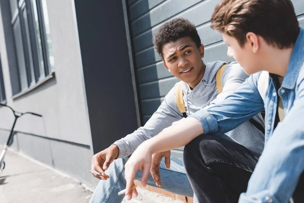 Gutaussehende und brünette Jungen sitzen, reden und rauchen Zigaretten — Stockfoto