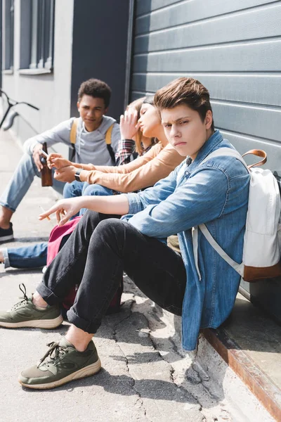 Jugendliche sitzen, trinken Bier aus Glasflasche und halten Zigarette — Stockfoto