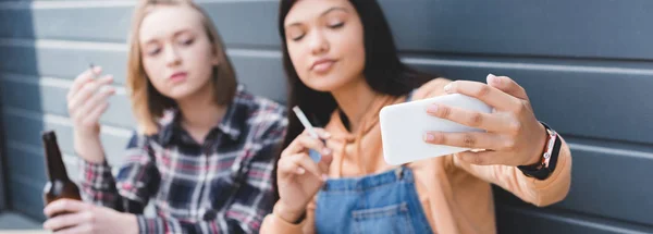 Foto panorámica de amigos guapos fumando cigarrillos y tomando selfie - foto de stock