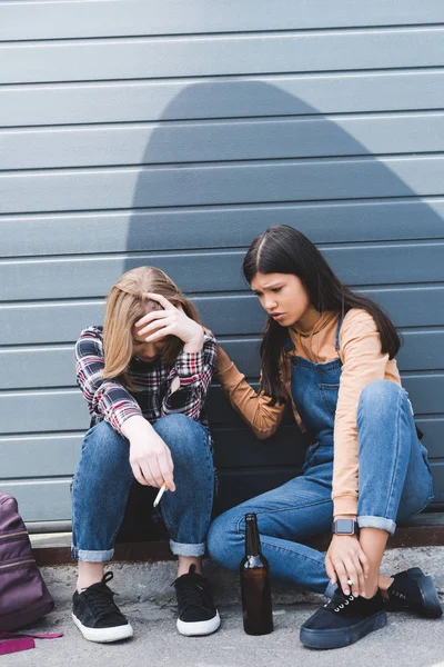 Adolescenti tristi e carini seduti, parlando e tenendo in mano le sigarette — Foto stock
