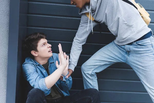 Cropped view of african american boy in hoodie and jeans punching scared boy — Stock Photo