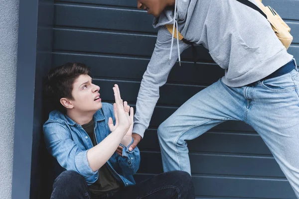 Abgeschnittene Ansicht eines afrikanischen amerikanischen Jungen in Kapuzenpulli und Jeans, der einen verängstigten Jungen schlägt — Stockfoto