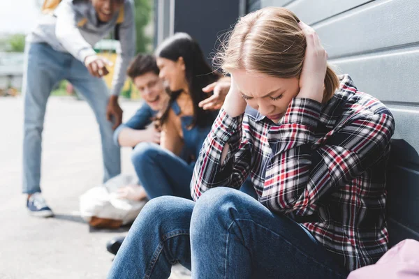 Enfoque selectivo de amigos sonrientes acosando y señalando con los dedos a la triste rubia adolescente - foto de stock