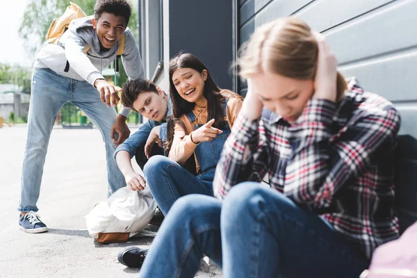 Pretty and smiling friends bulling and pointing with fingers at sad blonde teen — Stock Photo