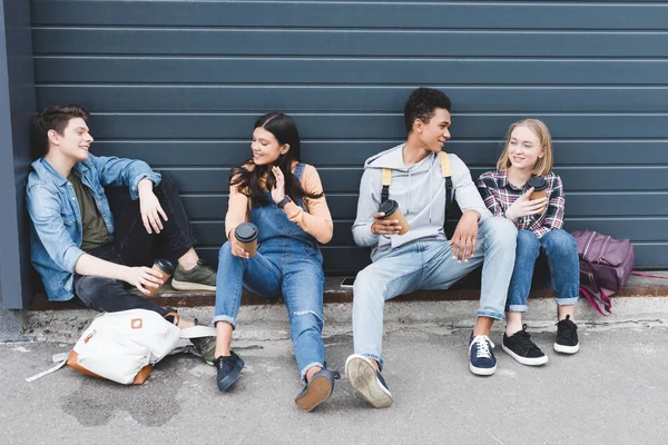 Jugendliche sitzen, trinken Kaffee aus Einwegbechern und reden — Stockfoto