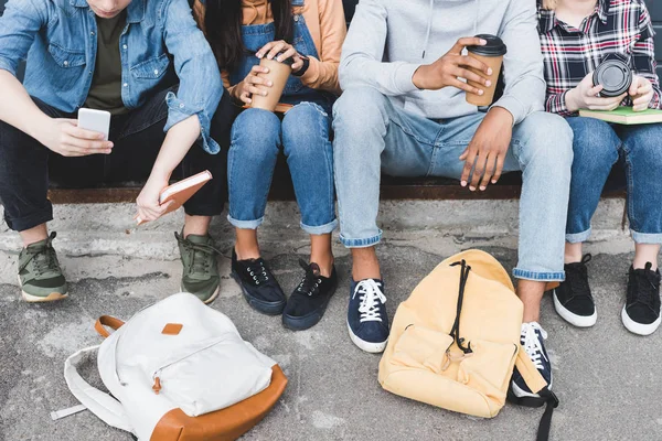 Vista recortada de los adolescentes sentados, beber café de tazas desechables y el uso de teléfonos inteligentes - foto de stock