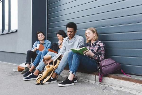 Adolescents assis, parlant, tenant des tasses en papier et lisant des livres — Photo de stock