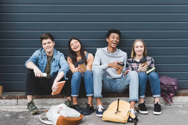 Adolescents heureux assis, souriant, tenant des tasses en papier et regardant la caméra — Photo de stock