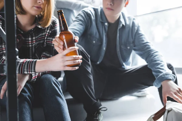 Vista ritagliata del ragazzo dando bottiglia di vetro di birra alla ragazza bionda — Foto stock