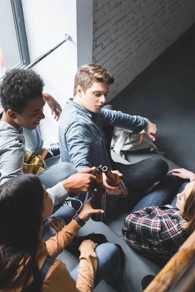 High angle view of smiling teenagers sitting on stairs and clinking — Stock Photo