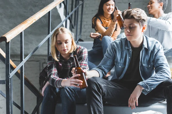 Adolescentes sentados en las escaleras, sosteniendo botellas de vidrio y hablando - foto de stock