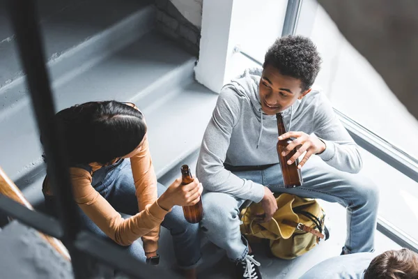 High angle view of teenagers talking, sitting on stairs and holding beer — Stock Photo