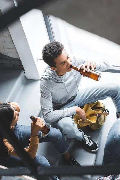 High angle view of teenagers talking, sitting on stairs and drinking beer — Stock Photo
