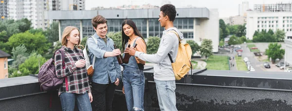 Panoramic shot of smiling teenagers clinking and smoking cigarette — Stock Photo