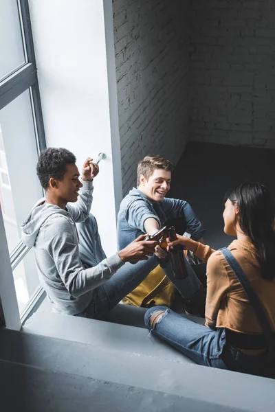 Positive and happy teenagers sitting on stairs, smiling and clinking — Stock Photo