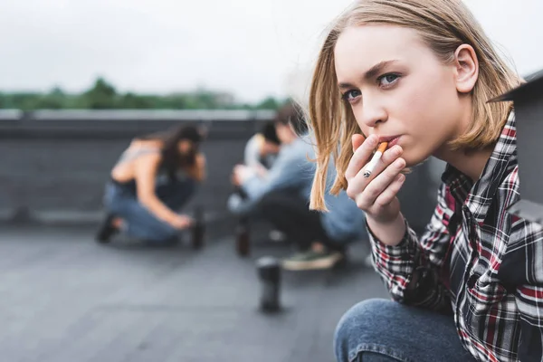 Selective focus of pretty and blonde teen smoking cigarette and looking away — Stock Photo