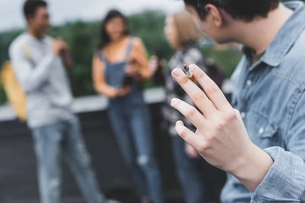 Enfoque selectivo de fumar cigarrillo adolescente con amigos en el techo - foto de stock