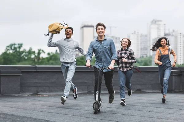 Playful and smiling teenagers running on roof and riding scooter — Stock Photo