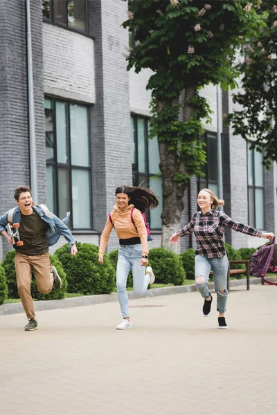 Adolescentes brincalhões e felizes correndo com skate e sorrindo — Fotografia de Stock