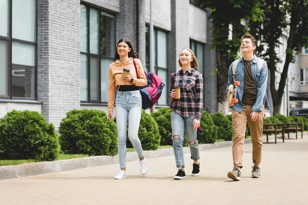 Smiling teenagers walking, holding disposable cups, looking away — Stock Photo