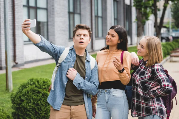 Happy teenagers holding smartphone, taking selfie and smiling — Stock Photo