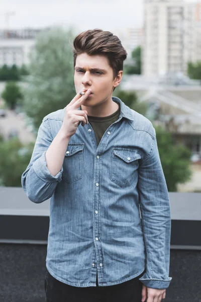 Caucásico adolescente en denim camisa fumar cigarrillo en el techo - foto de stock