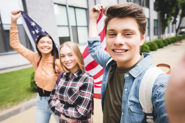 Adolescentes sorrindo tirar selfie e segurando bandeira americana fora — Fotografia de Stock