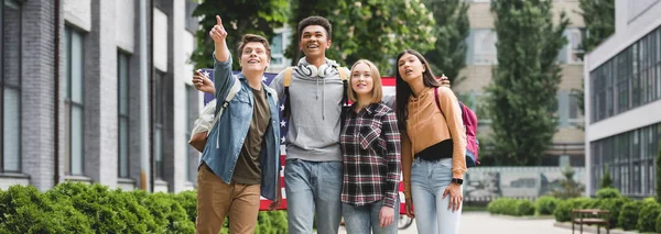 Plano panorámico de adolescentes sosteniendo bandera americana y señalando con el dedo - foto de stock