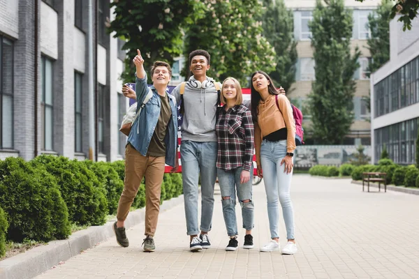 Adolescentes felices sosteniendo bandera americana y señalando con el dedo - foto de stock