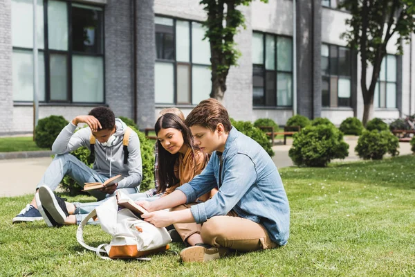 Teenagers sitting on green grass and reading books outside — Stock Photo