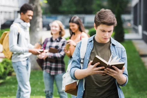 Foco seletivo do livro de leitura de adolescentes com amigos em segundo plano — Fotografia de Stock