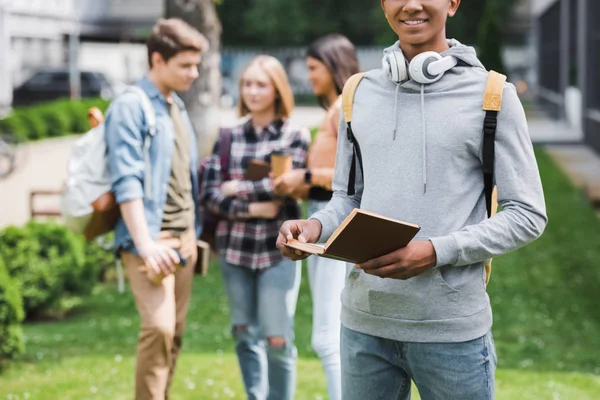 Cropped view of african american teenager in hoodie holding book — Stock Photo