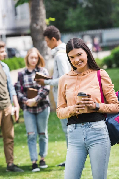 Adolescente sorrindo segurando copo de papel com café e olhando para a câmera — Fotografia de Stock