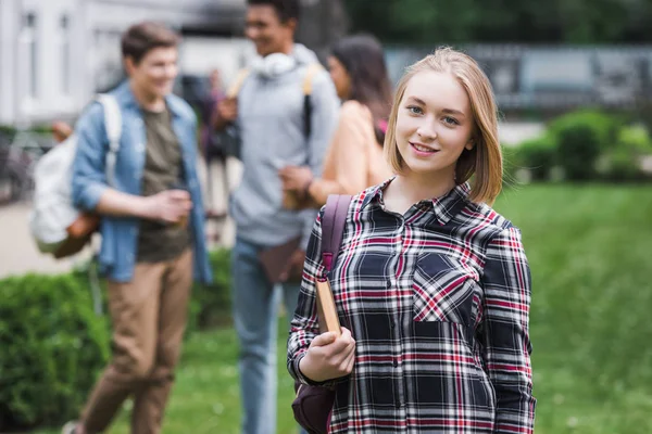 Lächelnder blonder Teenager mit Buch und Blick in die Kamera — Stockfoto
