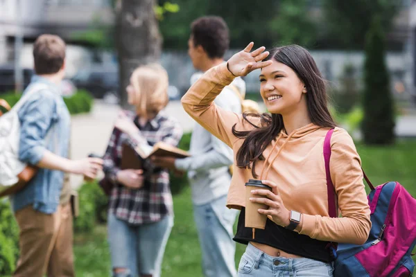 Smiling and brunette teenager holding paper cup with coffee and looking away — Stock Photo