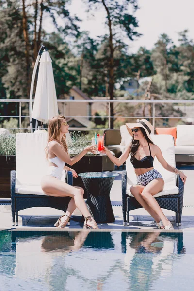 Щаслива брюнетка і блондинка в купальниках п'ють коктейлі біля басейну — стокове фото