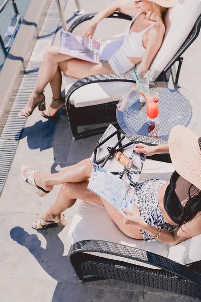 Vista aérea de mulheres sentadas perto da piscina e leitura de diários — Fotografia de Stock