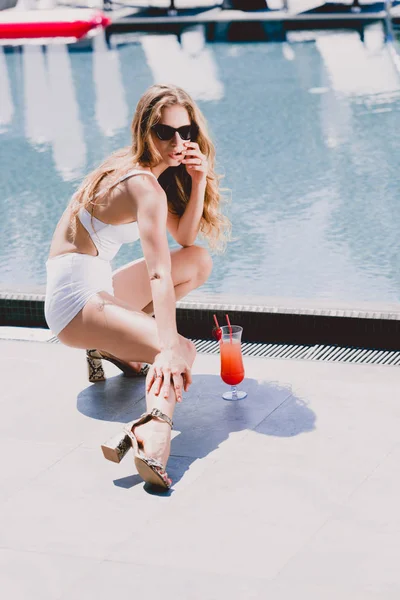 Sexy blonde model in swimsuit posing with cocktail near swimming pool — Stock Photo