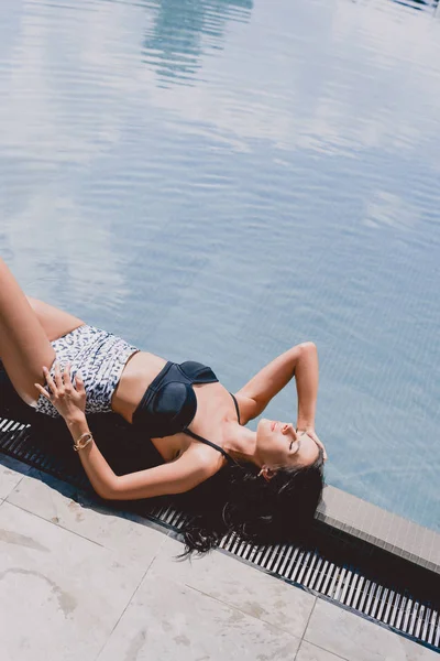 Mulher morena sexy em banho de sol maiô com olhos fechados perto da piscina — Fotografia de Stock