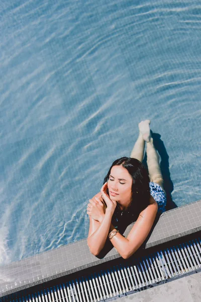 Hermosa morena húmeda mujer con los ojos cerrados tomar el sol en el agua en la piscina - foto de stock