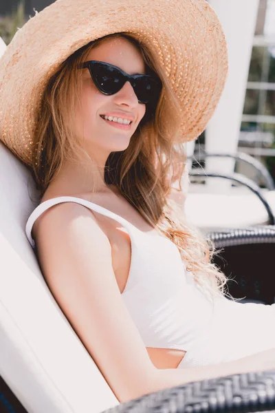 Mujer rubia feliz en sombrero de paja y gafas de sol tomando el sol en la tumbona - foto de stock