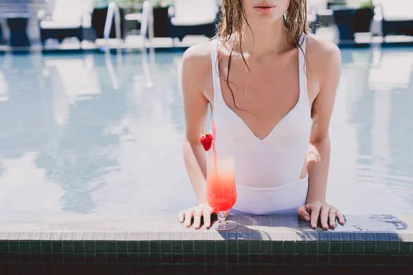 Обрезанный вид на мокрую женщину в бассейне с прохладным клубничным коктейлем — стоковое фото
