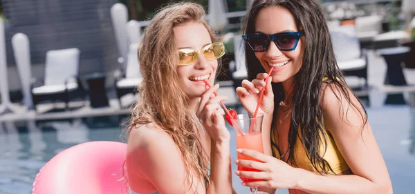 Smiling friends in sunglasses drinking cocktail near swimming pool — Stock Photo